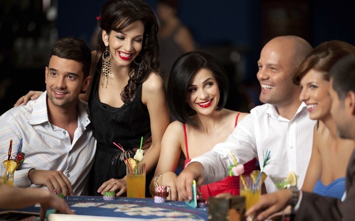 Двое азартных мужчин играют в казино за коктейлями, а женщины улыбаются им и заигрывают