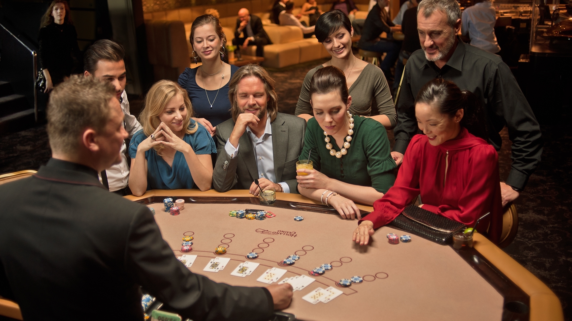 Элегантный дилер ведет игру в блэкджек для мужчины и троих женщин, а другие гости казино наблюдают за процессом
